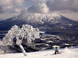 SJEZDOVÁNÍ U SOPKY. Snowboardista brázdí sjezdovku v lyaském areálu na...