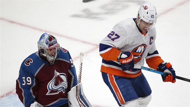 Pavel Francouz z Colorada vyr puk, ped jeho brankou clon Anders Lee z NY Islanders.