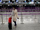 Cestující z Londýna nosí ochrannou rouku proti koronaviru na mezinárodním...
