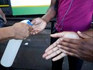 Zdravotnický pracovník dezinfikuje ruce cestujícím na autobusovém nádraí v...