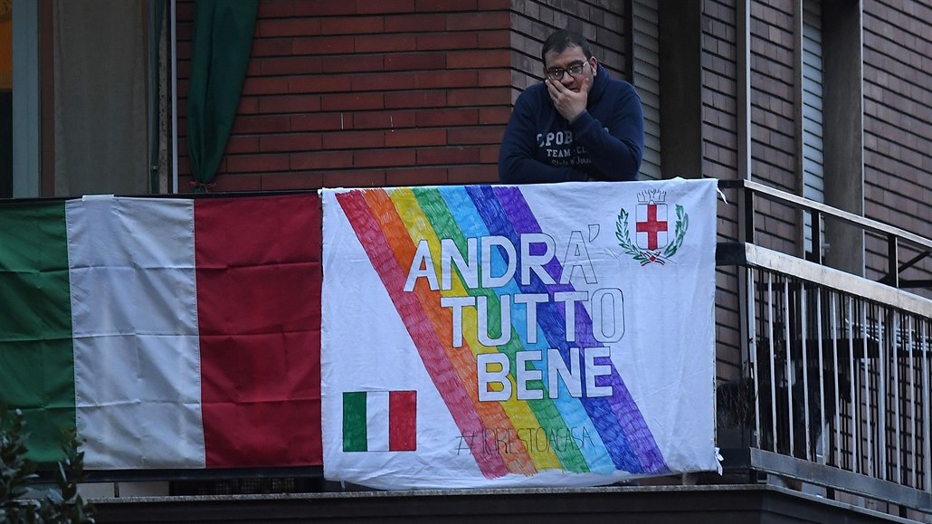 Muž sleduje dění na ulici ze svého balkonu. Prapor s nápisem „Andra Tutto Bene“...