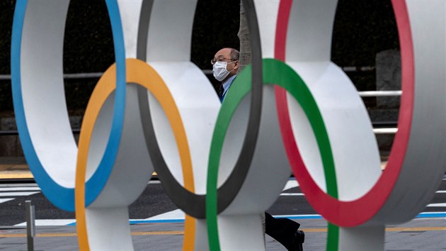 OLYMPIÁDA, NEBO KORONAVIRUS? Muž v roušce prochází kolem olympijských kruhů u tokijského olympijského muzea.