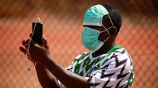 Mladý muž v ochranné roušce si fotí přátelské fotbalové utkání v nigerijské...