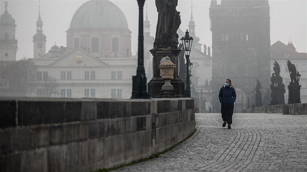 Turistka prochází po opuštěném Karlově mostě v Praze. (18. března 2020)