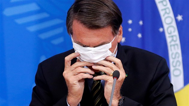 Brazilsk prezident Jair Bolsonaro bojuje s ochrannou roukou bhem tiskov konference. (18. bezna 2020)