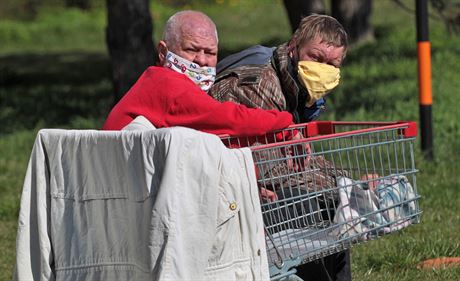 Bezdomovci v roukách sedí na lavice v Ostrav Hrabvce. (8. dubna 2020)