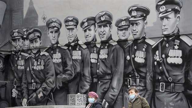 Dv Rusky s roukami na ochranu proti koronaviru ped poulinm graffiti zobrazujcm sovtsk hrdiny z druh svtov vlky. (3. dubna 2020)