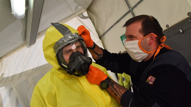 Jedna parta. Hasič (v tmavém) pomáhá bezpečně upevnit a zaizolovat masku záchranáři, který vyjíždí k případům COVID-19.