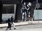 Obyvatelé Los Angeles prochází kolem pouliního graffiti s motivem koronavirové...