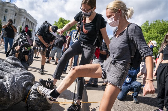 Demonstranti triumfáln pokládají nohy na svrenou sochu objevitele Ameriky...