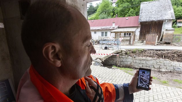 Petr Večeřa z Břevence ukazuje fotografii zachycující obří hráz, která se během bleskové povodně vytvořila před jeho domem z naplavených klad, které se zachytily a poté vzpříčily o mostek přes potok Dražůvka.