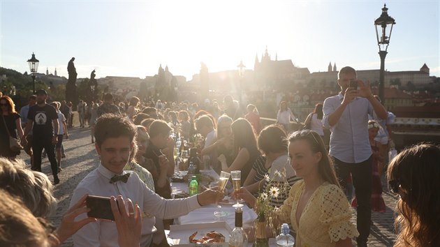 Lidé si užívají západ slunce na Karlově mostě při sousedském posezení u jednoho dlouhého stolu. (30. června 2020)