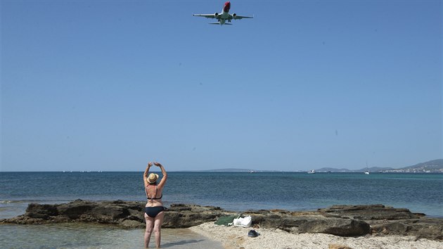 Návštěvnice pláže na španělském ostrově zdraví letadlo. Španělsko rozčílilo rozhodnutí britské vlády dát navrátilce ze Španělska zpět do čtrnáctidenní karantény. (29. července 2020)