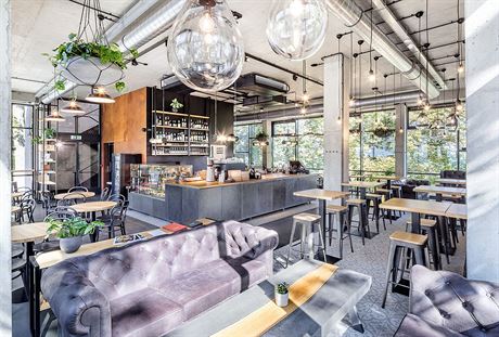 Industriální prostor nové kavárny je ze tí stran prosklený fasádními systémy.