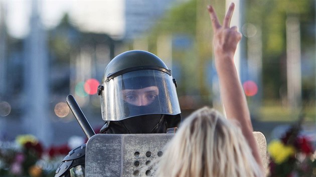 Neznámá žena ukazuje gesto vítězství běloruskému policistovi nedaleko místa, kde během protestů proti prezidentským volbám zemřel demonstrant. (11. srpna 2020)