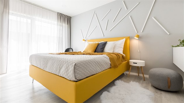 Ložnice má prostornou šatnu a jejím dominantním prvkem je zářivě žlutá postel s jednoduchou nástěnnou dekorací.