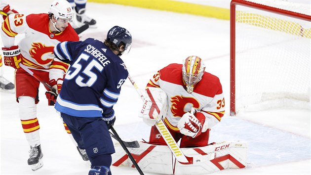 Brank Calgary David Rittich zasahuje, t se na nj centr Winnipegu Mark Scheifele.