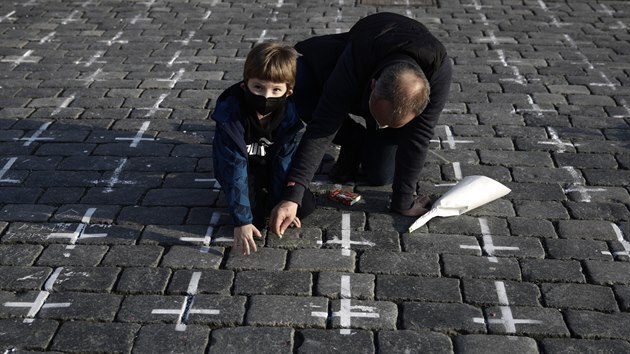 K namalovaným křížům na památku obětí koronaviru na Staroměstském náměstí v Praze lidé spontánně začali psát jména svých blízkých, kteří zemřeli a zapalovat svíčky. (24. března 2021)