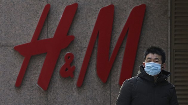 Muž s rouškou prochází kolem zavřené prodejny švédského řetězce společnosti H&M v Pekingu. Zavřené prodejny přinesly švédskému oděvnímu řetězci značné zrráty. (28. března 2021)