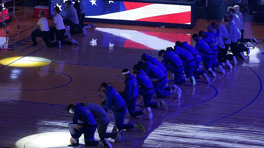 Hráči a trenéři Golden State Warriors klečí během poslechu hymny.