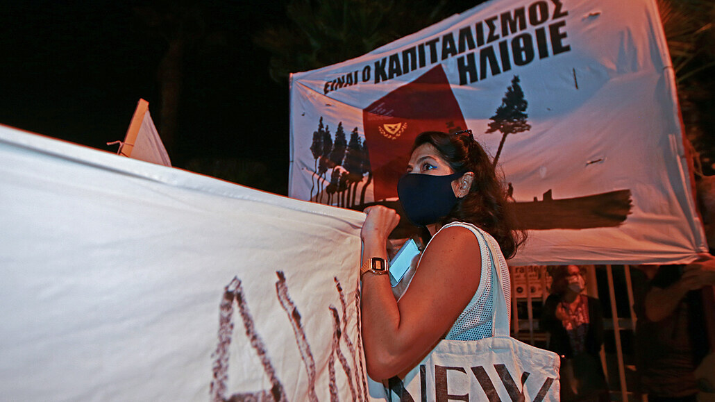 Demonstrant stojí před transparentem, který zní - v řečtině - „Je to...