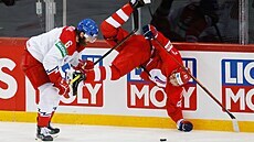 Ruský hokejista Konstantin Okulov padá krkolomně k ledu po střetu s Čechem...