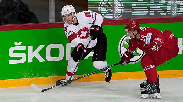 Švýcarský hokejista Christoph Bertschy hledá spoluhráče, v akci mu brání běloruský zadák Jevgenij Lisovec.