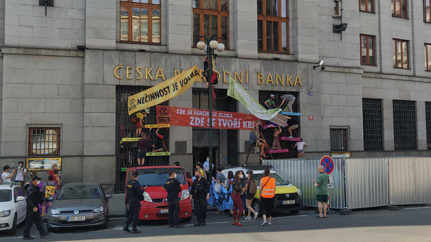 Aktivisté z Extinction Rebellion rozmisťují bannery nad vchodem do České národní banky. Přítomní policisté přihlížejí. (28. června 2021)