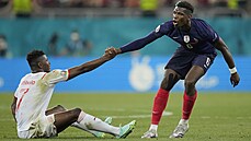 Paul Pogba (Francie) zvedá z trávníku výcara Breela Embola.