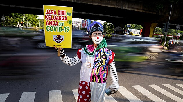Dobrovolnk ze skupiny Jsem indonsk klaun dr plakt na podporu osvtov kampan vyzvajc k noen ochrann masky na run kiovatce v indonsk Jakart. (12. ervence 2021)