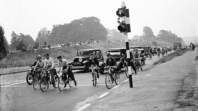 Kolona aut a cyklist ek na zelenou.
(1935)