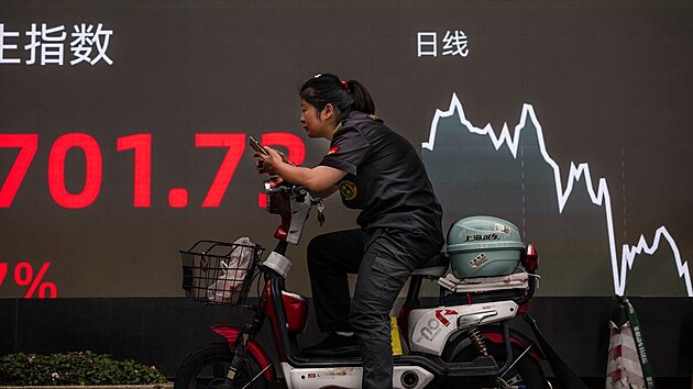 Za ženou na skútru v Šanghaji stojí obrazovka zobrazující nejnovější burzovní a ekonomická data. Akciovým trhem zmítají obavy kvůli dluhové krizi čínských developerů. (7. října 2021)