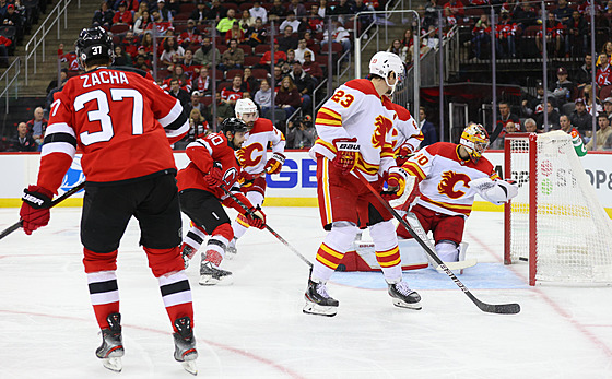 Pavel Zacha z New Jersey sleduje puk míící do branky Calgary. Daniel Vlada se...