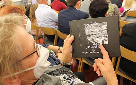 Žena ukazuje titulní snímek knihy z místa, které je nedaleko  jejího domova.