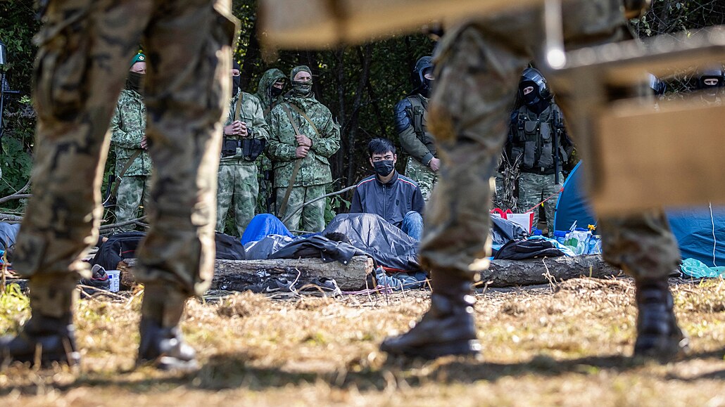 Polští (vpředu) a běloruští vojáci (v pozadí) hlídají skupinu migrantů...