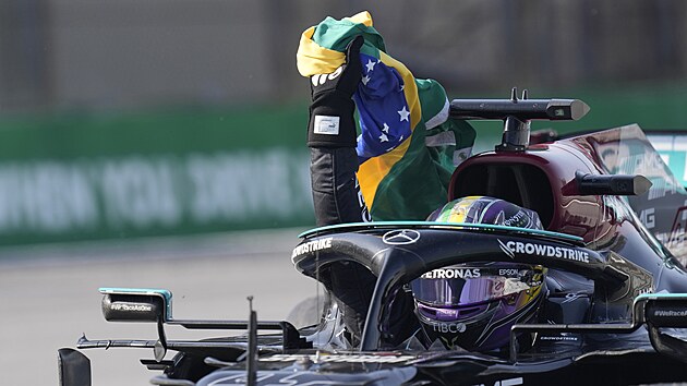 Lewis Hamilton slav s brazilskou vlajkou po svm triumfu na okruhu v Sao Paulu.
