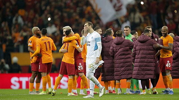 Zklamaný brankář Pau Lopez z klubu Olympique Marseille opouští trávník, zatímco se v pozadí radují z vítězství hráči Galatasaray Istanbul.