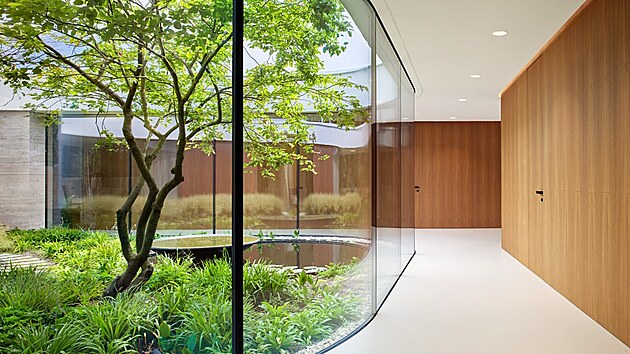 Celý interiér kombinuje přírodní travertin, dřevo ve výrazném odstínu a jednolitou světlou podlahu.