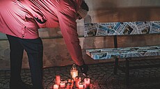 Lidé u lavičky Václavu Havlovi zapalují svíčky.