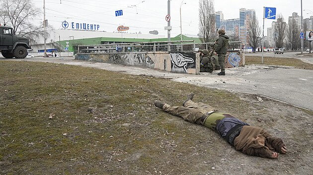 Tlo zabitho vojka le na zemi vedle skupinky ukrajinskch vojk. Rusk ozbrojen sly vstoupily do Kyjeva. (25. nora 2022)