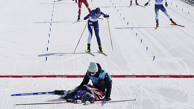 Američanka Jessie Digginsová leží na sněhu po závodu na 30 kilometrů volnou technikou v Pekingu. Za ní dobíhá Finka Kerttu Niskanenová.
