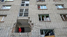 Ukrajinka vyhlíží z poničené budovy, která byla zasažena ruským minometem v...