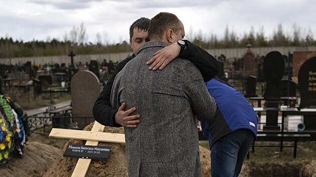 Muž z Buče se objímá s příbuzným u hrobu matky, která zemřela v domově důchodců kvůli špatným životním podmínkám během ruské invaze. (12. dubna 2022)
