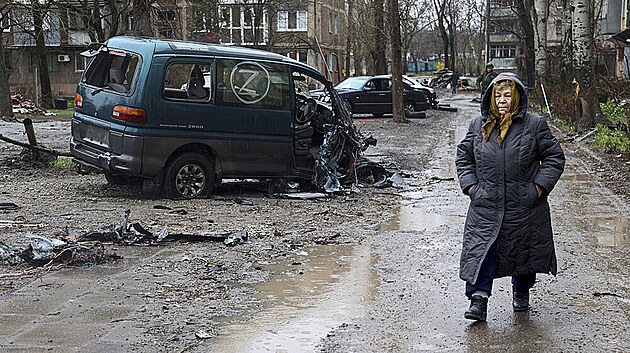 Obyvatelka Mariupolu prochází kolem zničeného auta s ruským označením Z. (13. dubna 2022)