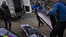 Pracovníci hřbitova v Buči ukládají mrtvé do rakví. (11. dubna 2022)