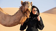 ena v emirátském národním odvu (abája) s velbloudem v poutních dunách Empty...