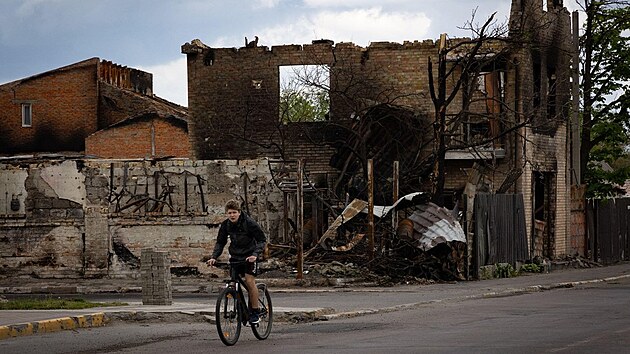 Chlapec projíždějící kolem zničeného domu v ukrajinské Buči (17. května 2022)
