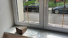 Rozbité okno i s dlažební kostkou, která do domu přiletěla.