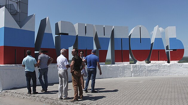 Skupina lidí prochází kolem nového cedule s názvem města v barvách ruské vlajky u vjezdu do Mariupolu. (12. června 2022)