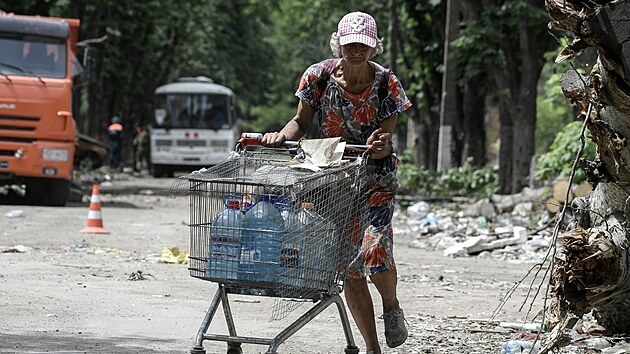 Obyvatelka Mariupolu jde po ulici s košíkem naplněným kanystry s vodou. (6. června 2022)
